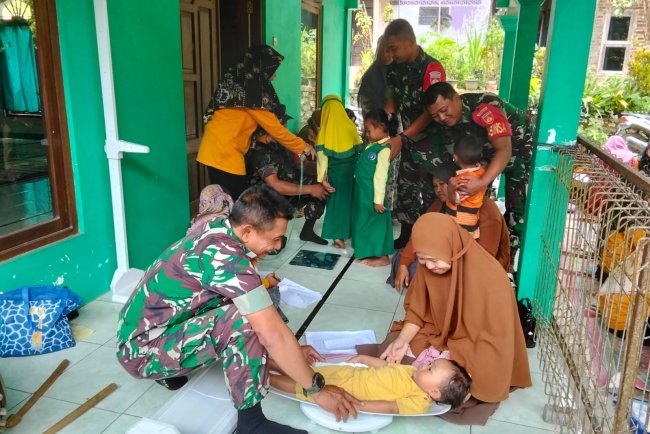 Danramil beserta Babinsa membantu kader dan bidan desa melaksanakan Posyandu Balita